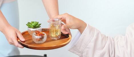 Una persona sosteniendo una bandeja con un vaso de líquido ámbar, una pequeña suculenta y un vaso transparente con un diseño dorado.