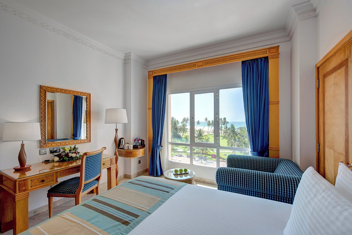 Una habitación de hotel con cama, escritorio, silla, una mesita y ventana con cortinas.