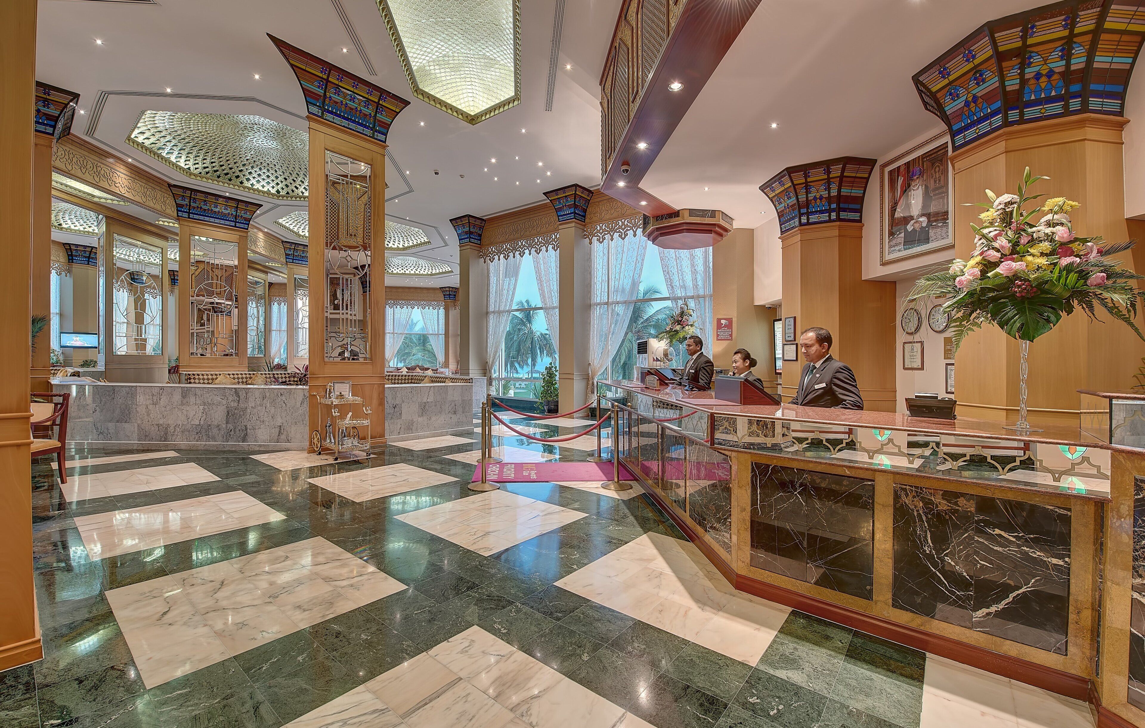 A hotel lobby with a marble floor, a reception desk, and a large window with a view of palm trees.