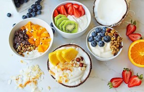 Tre skåle med yoghurt toppet med forskellige frugter og nødder.