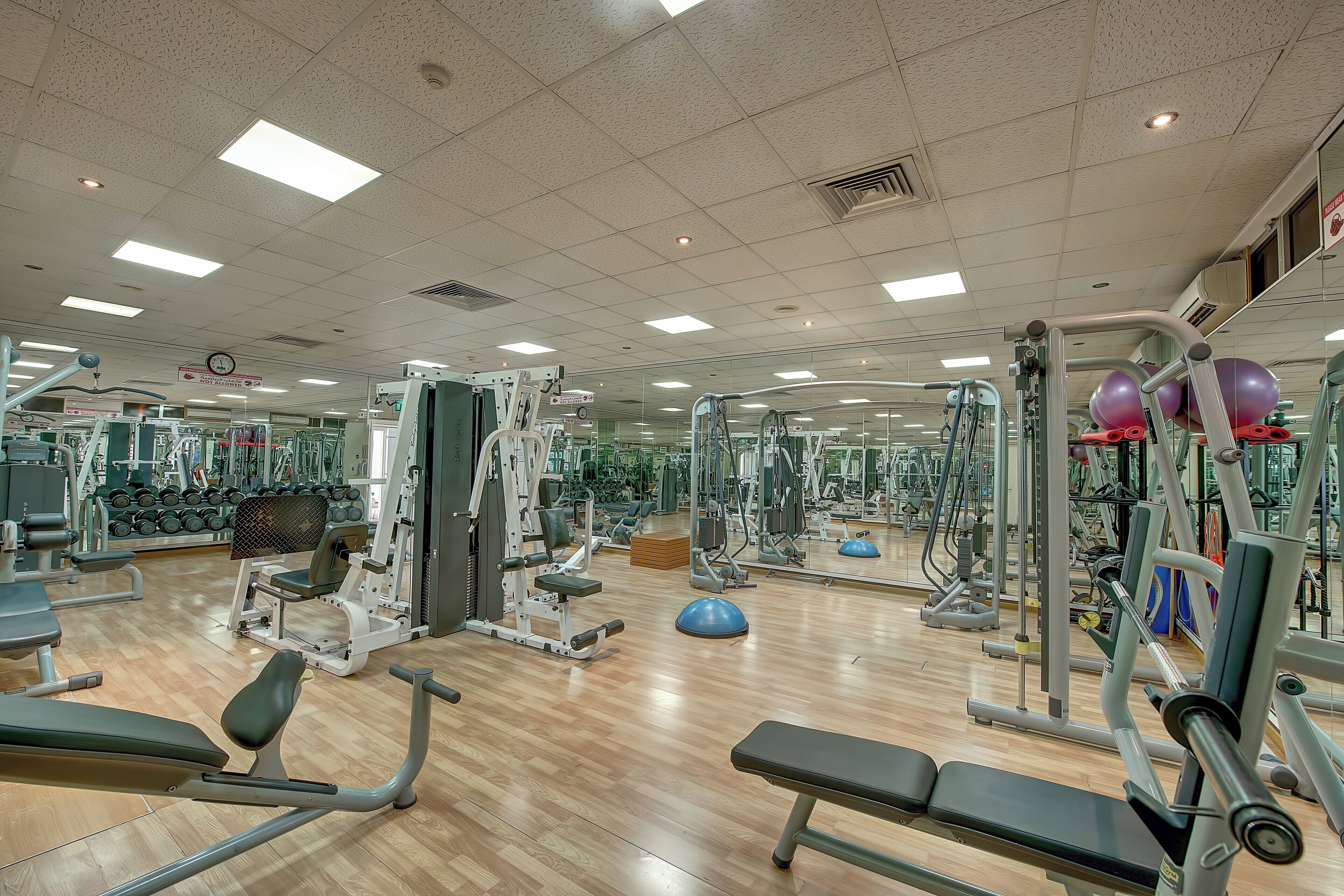 Un gimnasio con diversos equipos de ejercicio, suelo de madera y un espejo grande.