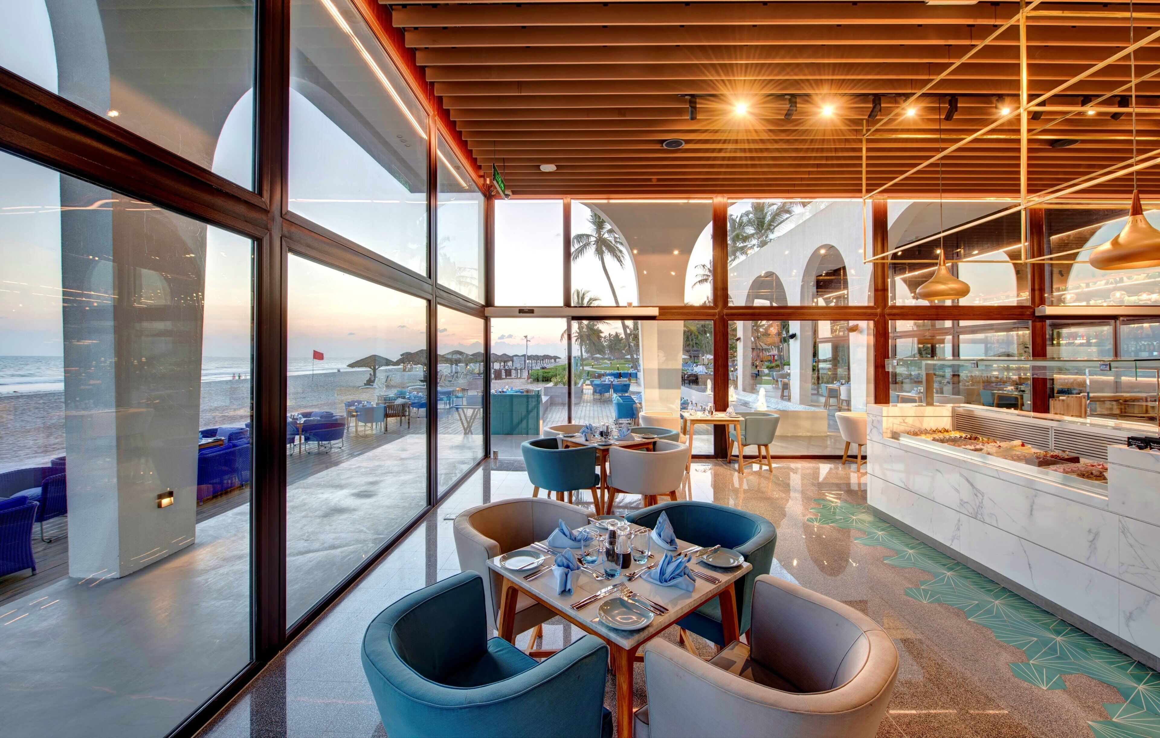 A restaurant with a view of the beach, large windows, and modern furniture.