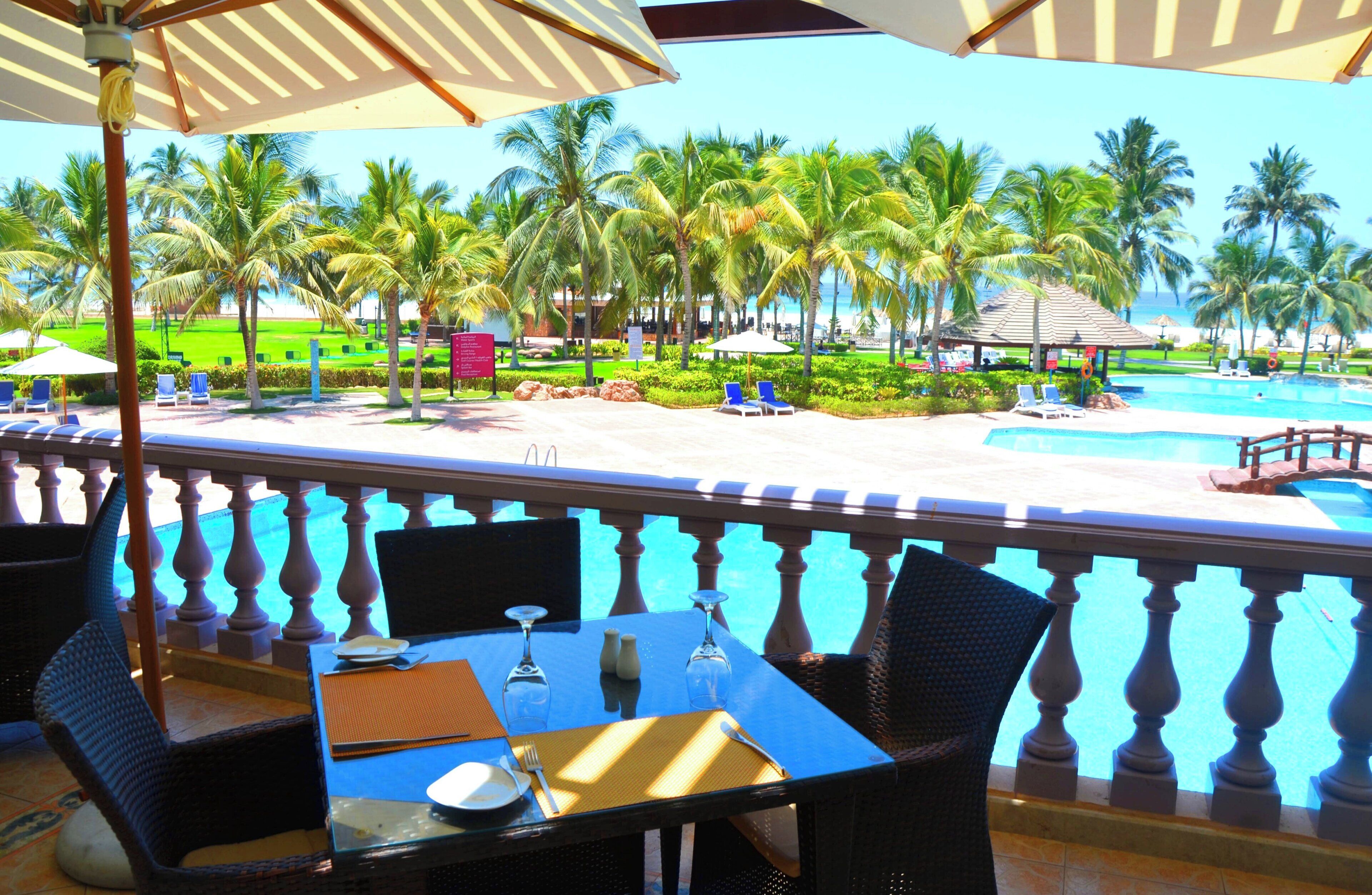 A poolside view with a table set for dining, overlooking a pool area with lounge chairs and palm trees.