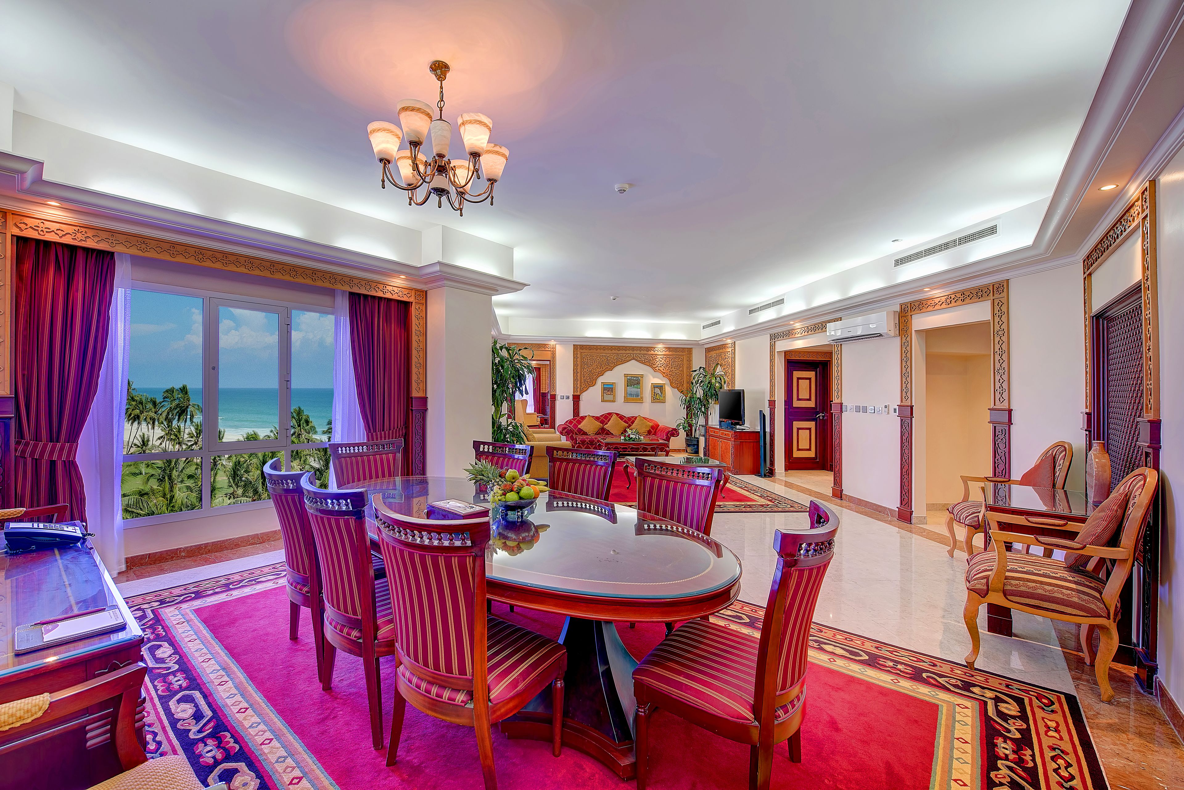 A spacious dining area with a round table and chairs, large windows with curtains, and a view of the ocean.