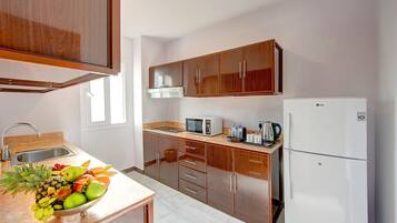 A kitchen with wooden cabinets, a microwave, a refrigerator, and a fruit bowl on the counter.