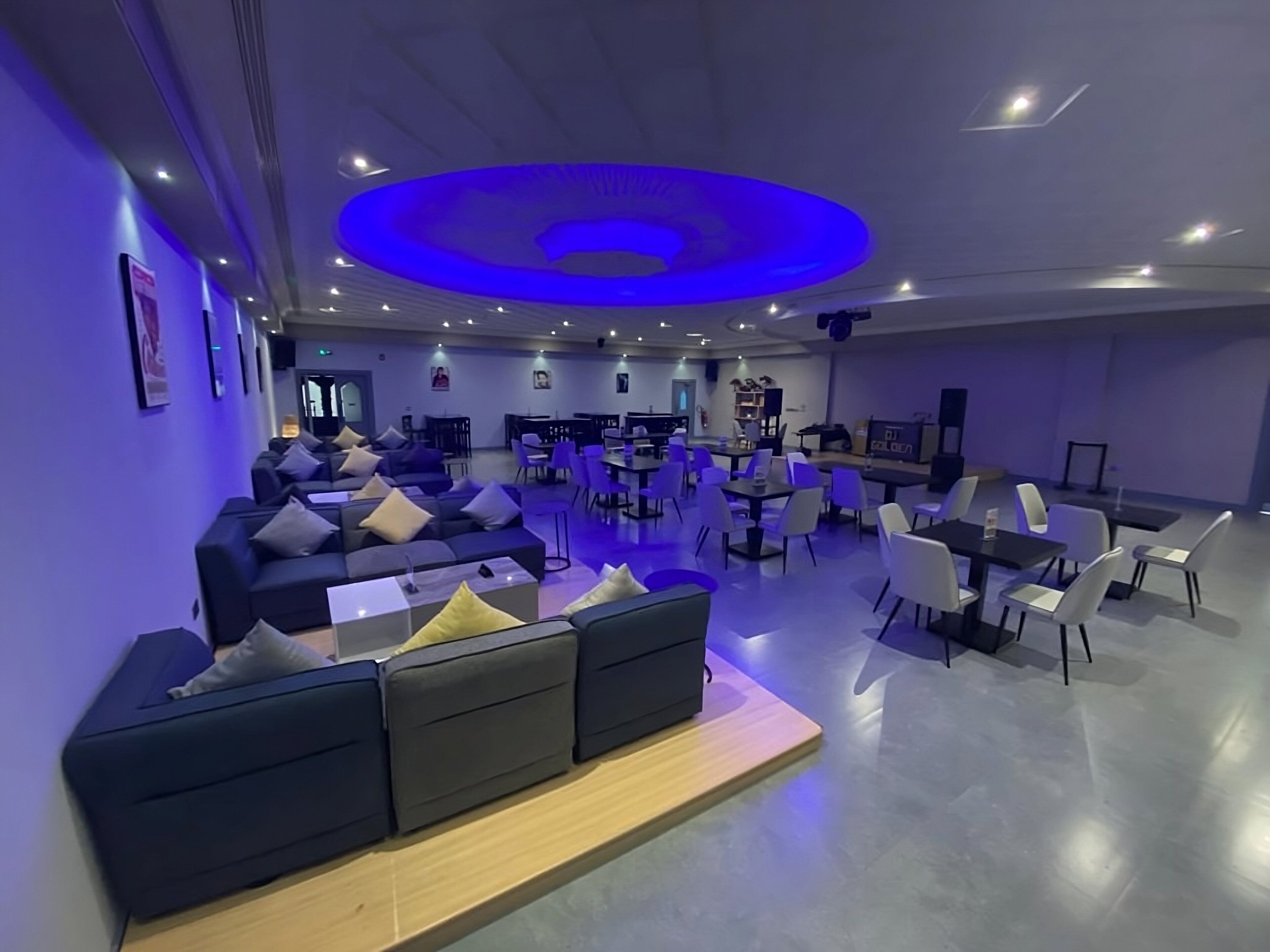 A modern lounge area with sofas, tables, and chairs, featuring a central circular light fixture.