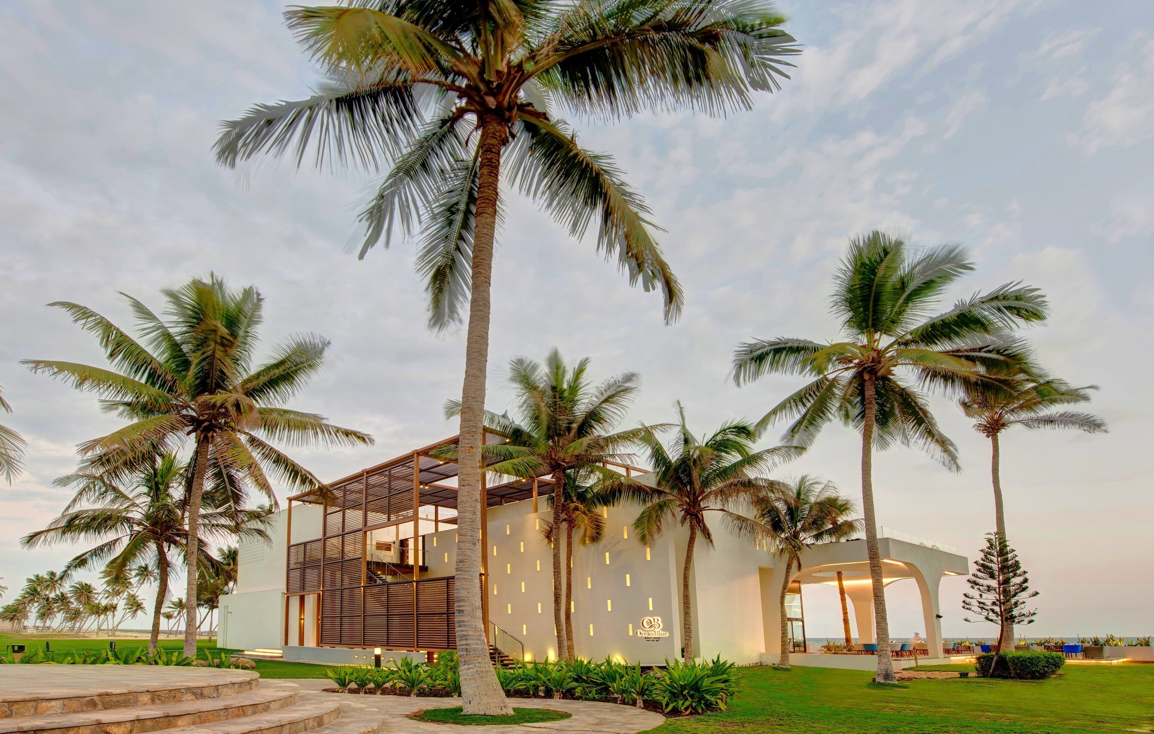 A modern building with a glass facade, surrounded by palm trees and a well-maintained lawn.