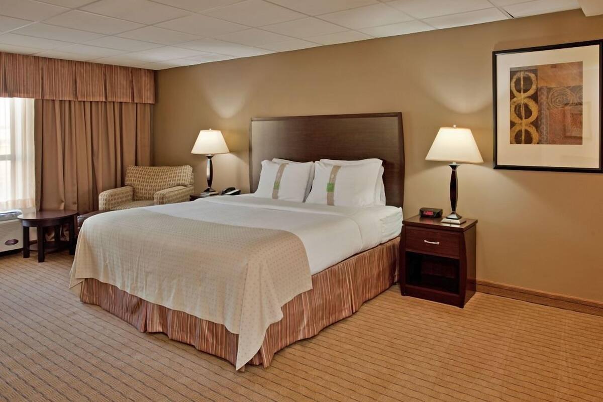 A hotel room with a large bed, two bedside tables, a chair, a lamp, and a framed picture on the wall.