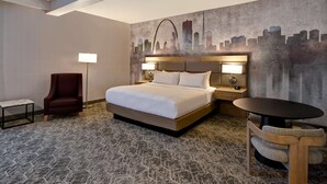 A hotel room with a large bed, a chair, a table, and a cityscape mural on the wall. - DoubleTree by Hilton St. Louis Airport (St. Louis)