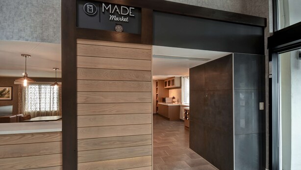 A modern interior with a wooden panel wall, a kitchen area, and a dining space with pendant lighting. - DoubleTree by Hilton St. Louis Airport (St. Louis)