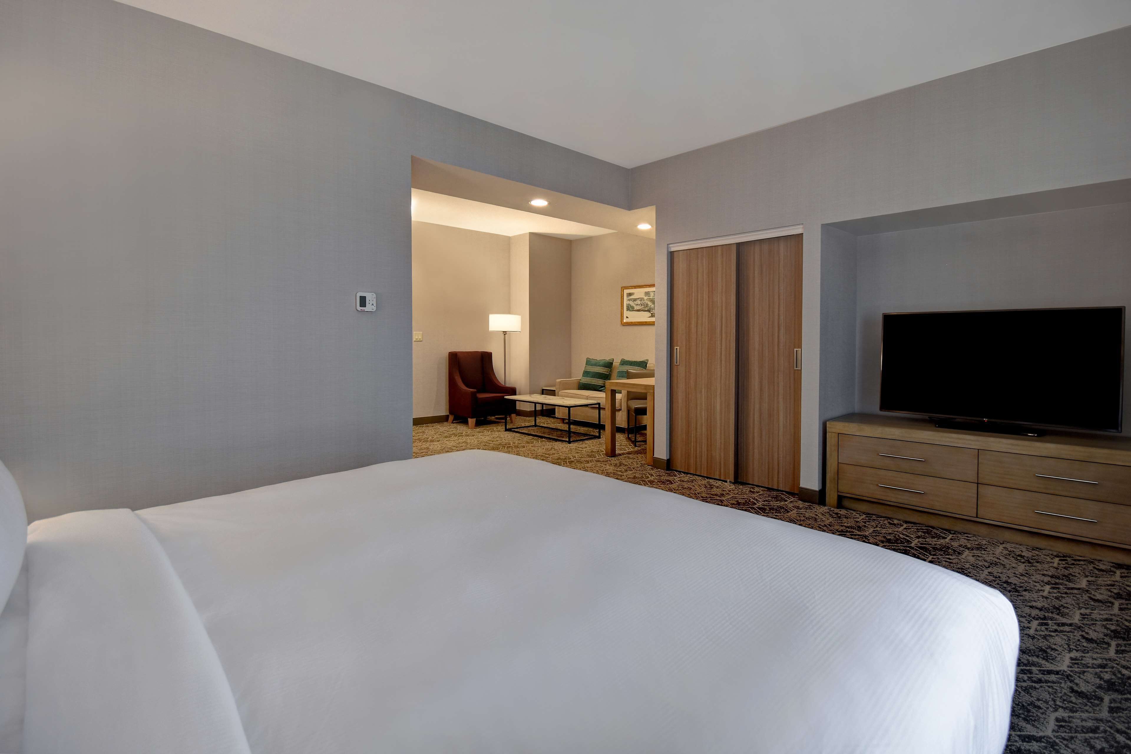 Ein Hotelzimmer mit einem großen Bett, einem Fernseher, einem Schreibtisch und einem Sessel.