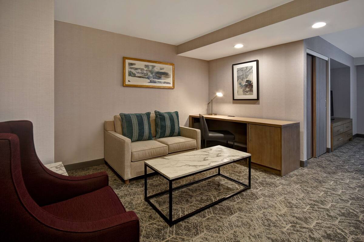 A modern living room with a sofa, a red armchair, a coffee table, a desk, and a computer. There are two framed pictures on the wall.