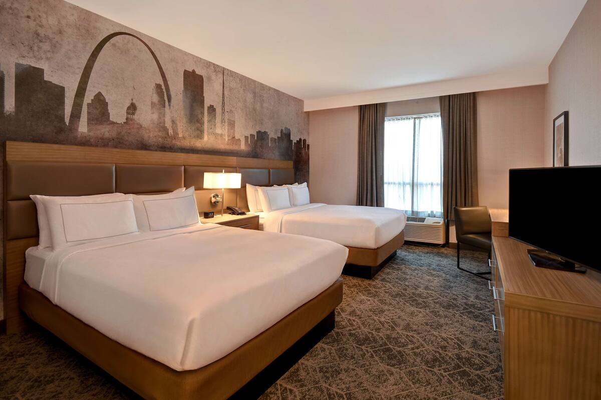 A hotel room with two beds, a large wall mural, a TV, and a desk.