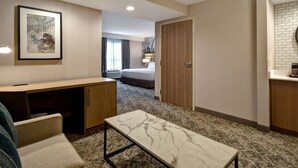 A hotel room with a bed, a desk, a chair, a small table, a framed artwork, and a bathroom with a mirror and sink. - DoubleTree by Hilton St. Louis Airport (St. Louis)