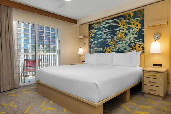 Een hotelkamer met een groot bed, een nachtkastje, een wandlamp en uitzicht op een gebouw door een glazen deur.