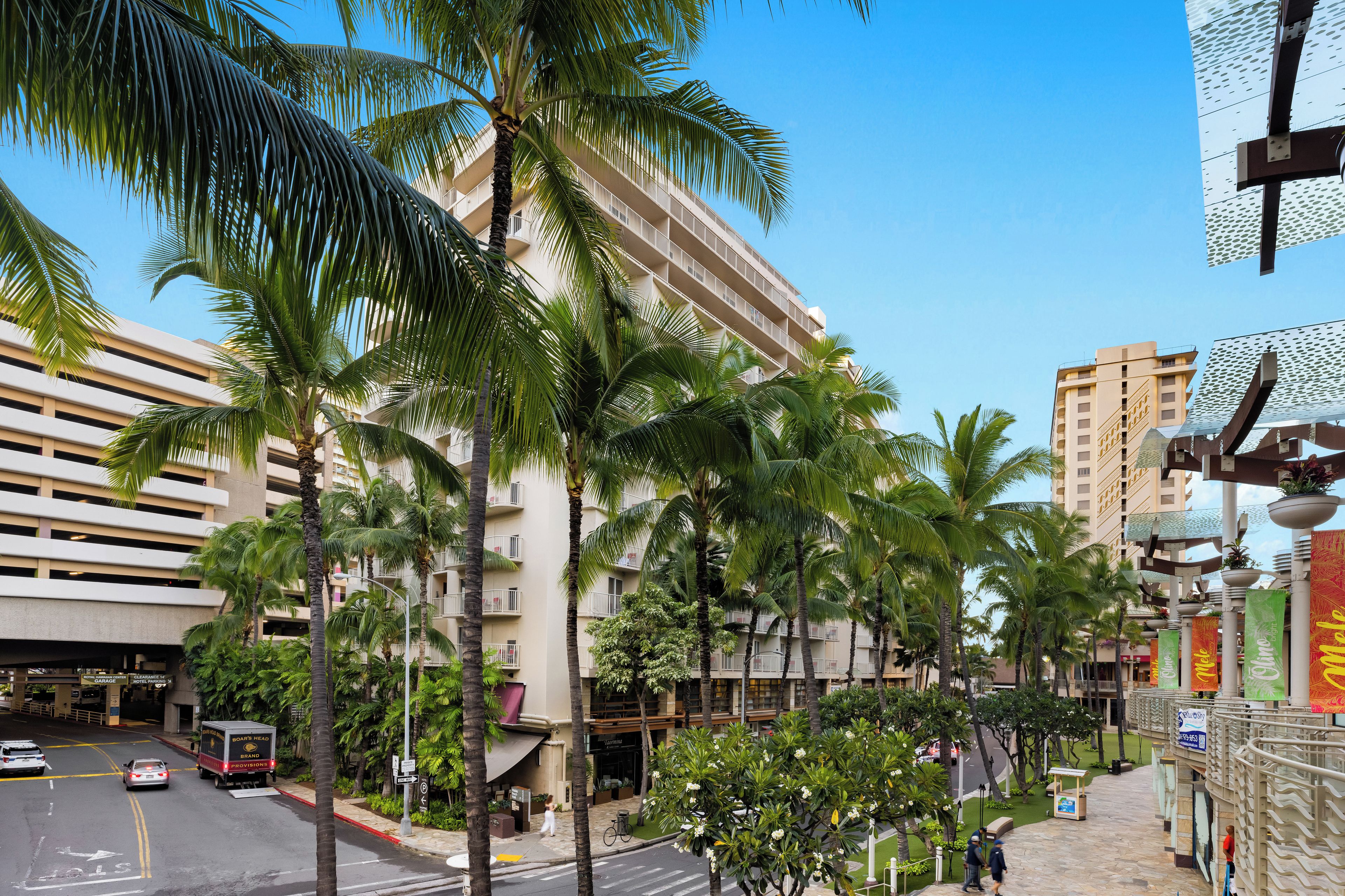 A multi-story hotel with balconies, palm trees, and a clear blue sky.