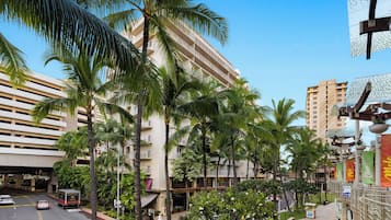 Un hotel de varios pisos con balcones, palmeras y un cielo azul despejado.