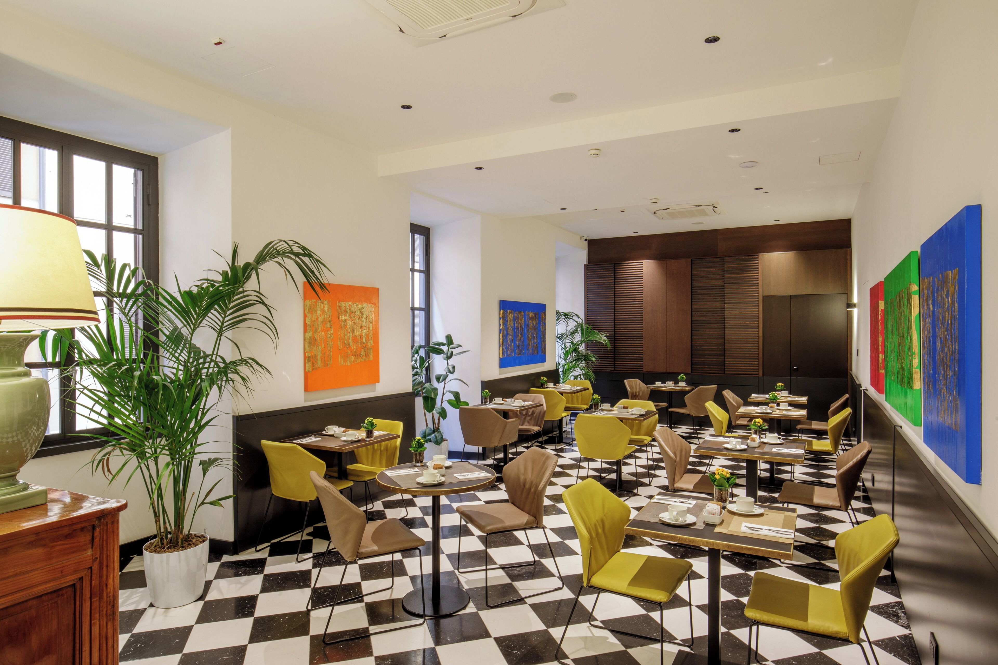 A modern dining area with checkered flooring, yellow chairs, and tables set for dining.