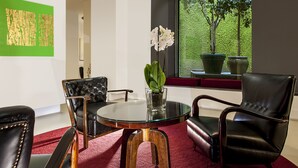 A modern room with a glass table, leather chairs, a vase with white flowers, and a view of trees through a window. - Hotel Nord Nuova Roma (Rome)