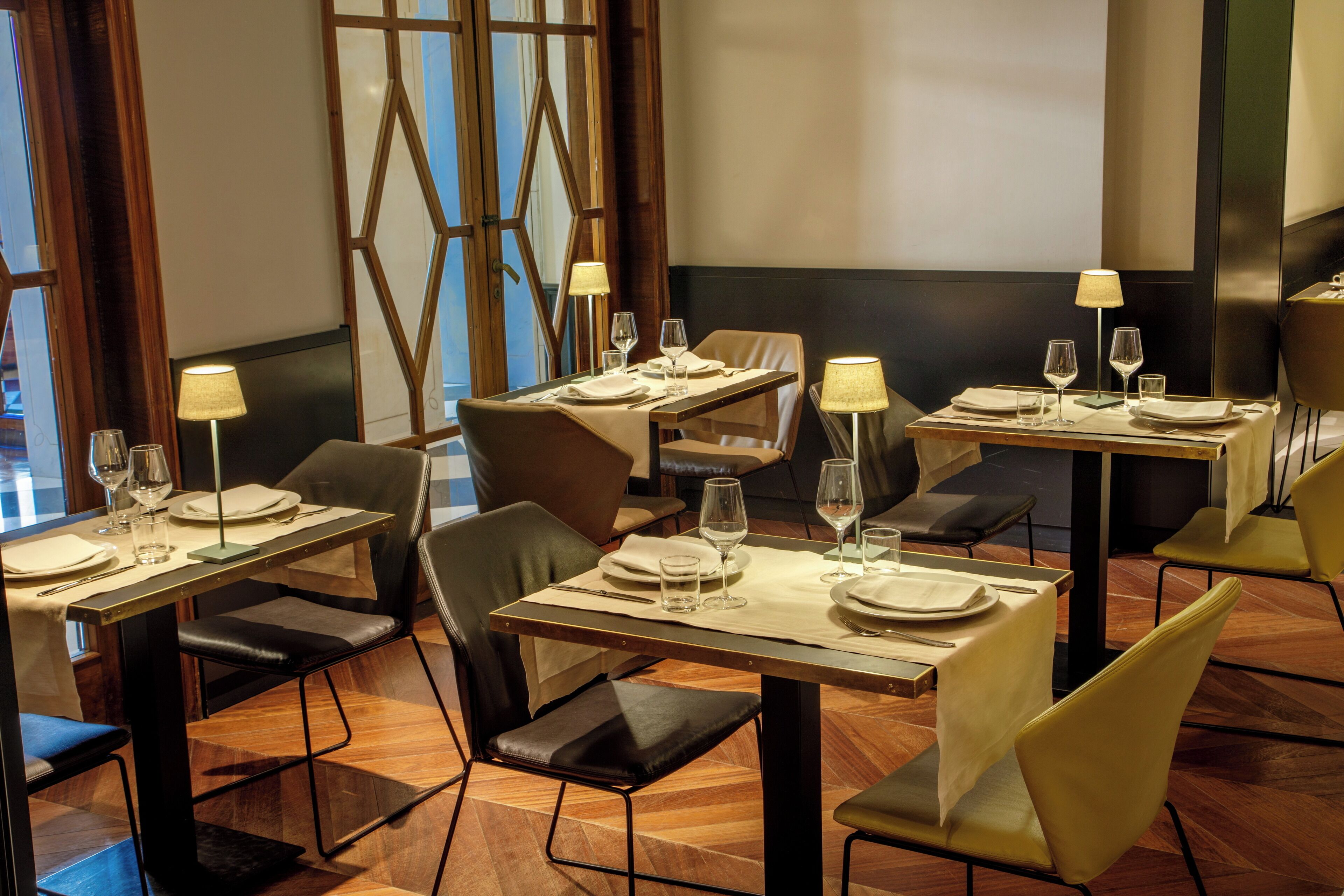 A restaurant with multiple tables set for dining, each with a tablecloth, plates, cutlery, and glasses.