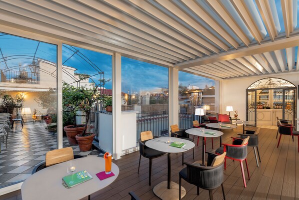 An outdoor patio area with round tables and chairs, large windows, and potted plants. - Hotel Nord Nuova Roma (Rome)