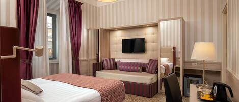 A hotel room with a bed, a sofa bed, a desk with a lamp, a television, and a coffee maker.