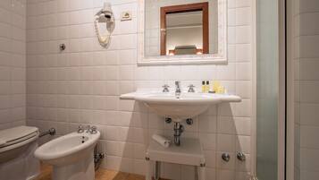 A bathroom with white tiles, a sink, a bidet, a toilet, and a mirror with a wooden frame.