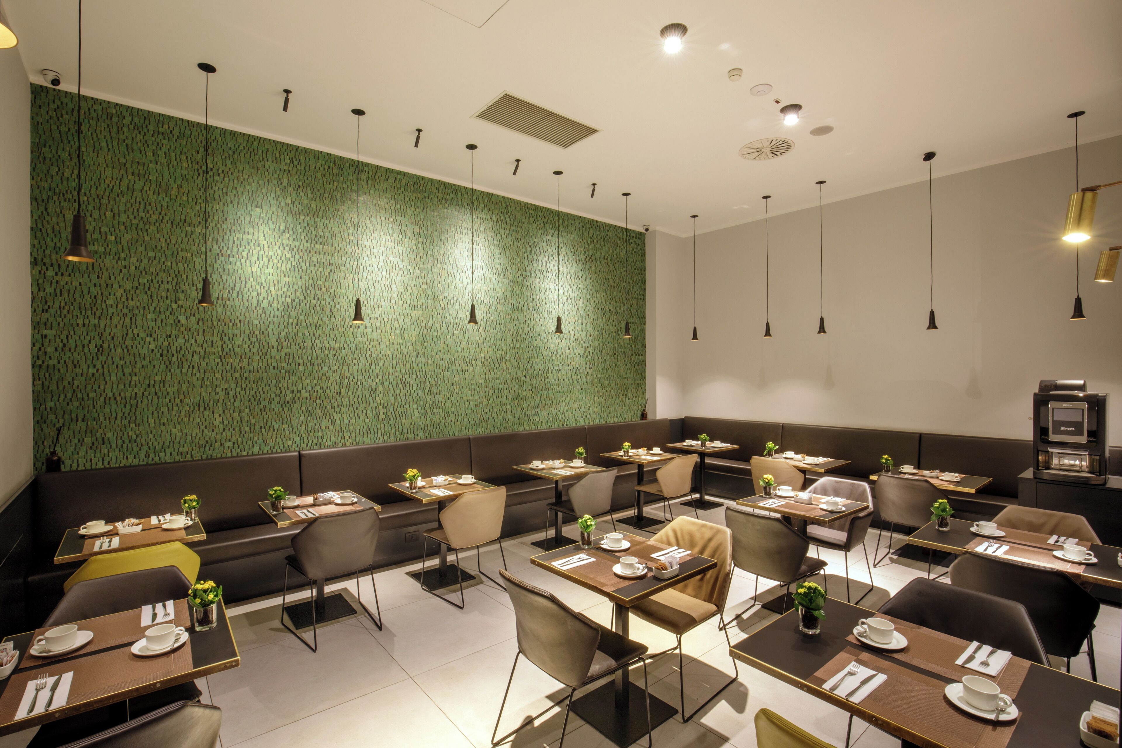 A modern restaurant with booths and tables, green textured walls, and pendant lighting.