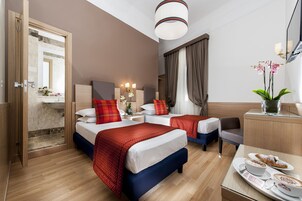Una camera d'albergo con due letti, una scrivania con una sedia, un bagno con doccia e una zona pranzo con tavolo imbandito per due persone.