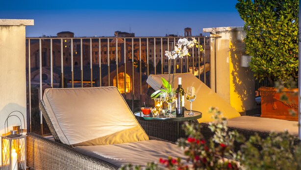 A balcony with wicker furniture, a table with drinks, and a view of buildings in the background. - Hotel Nord Nuova Roma (Rome)