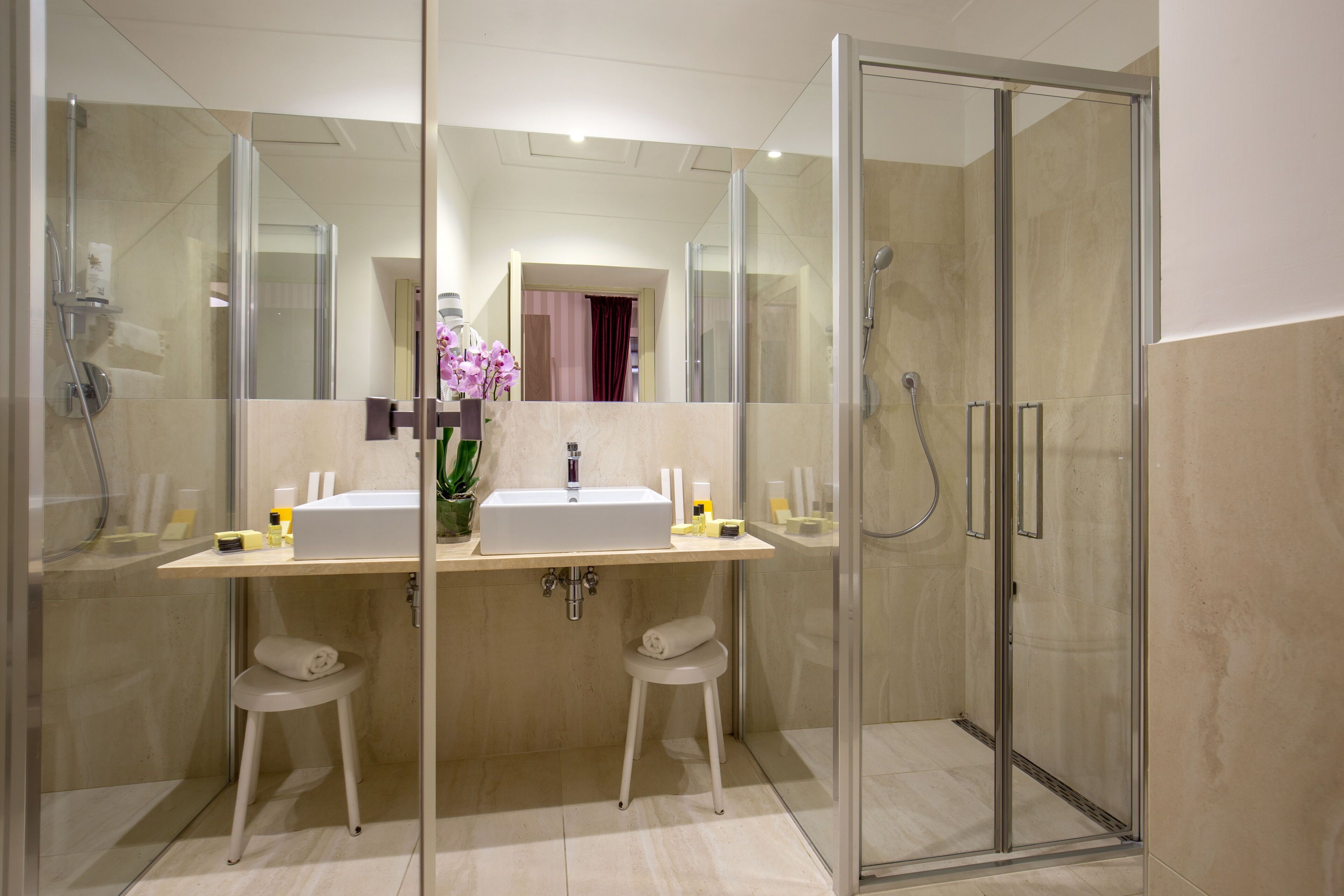 A modern bathroom with a glass-enclosed shower, two sinks, and a vanity with a mirror.