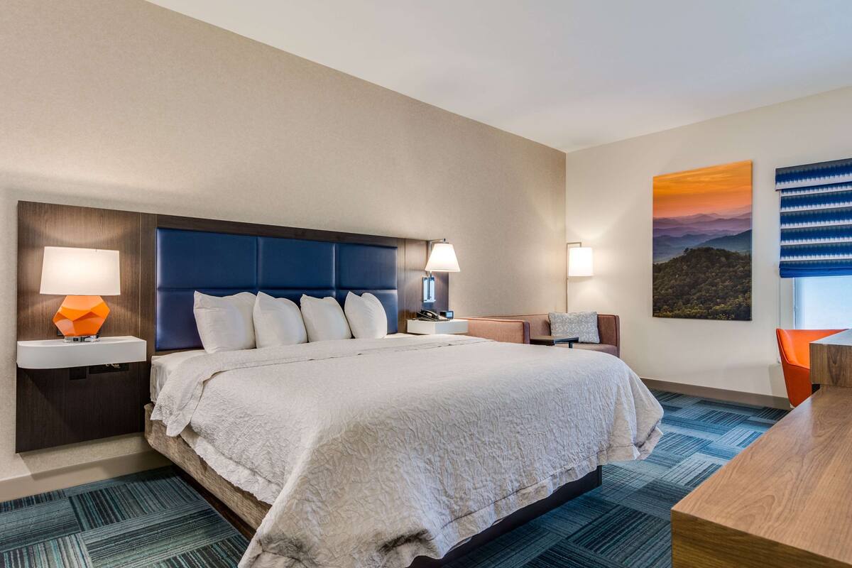 A hotel room with a large bed, two bedside tables, a nightstand, a desk, and a chair.