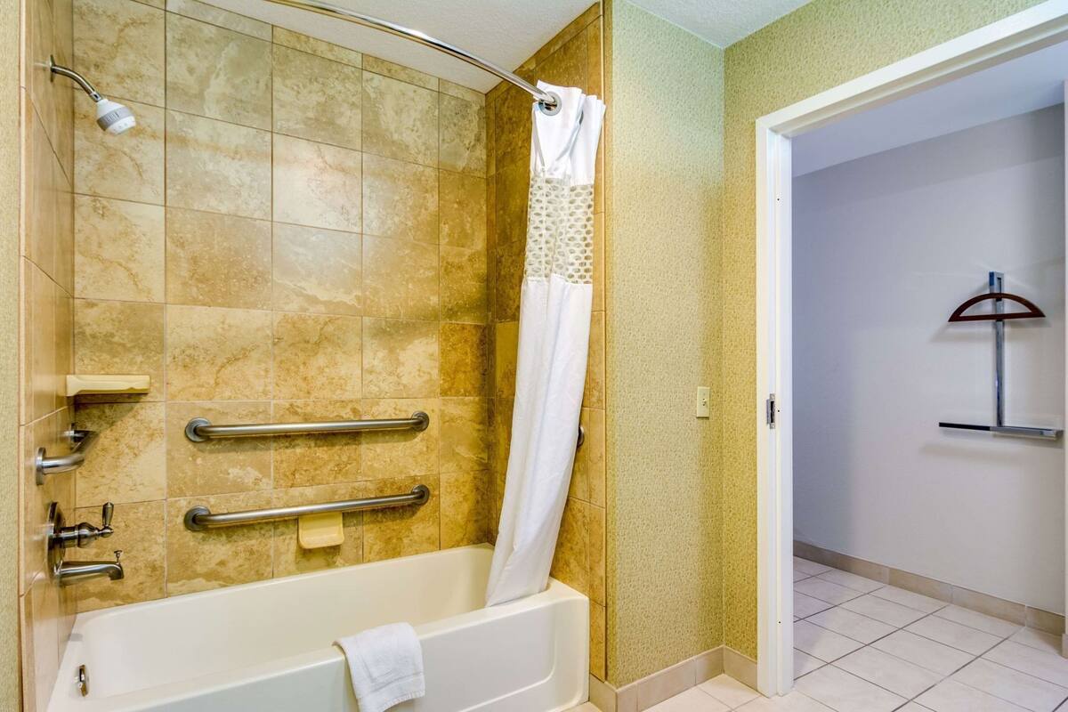 A bathroom with a bathtub, shower, grab bars, and a towel rack.
