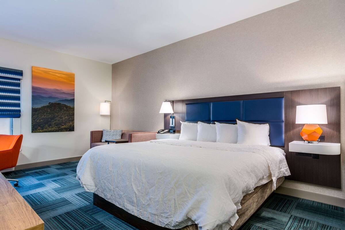 A hotel room with a large bed, two bedside tables with lamps, a wall-mounted TV, and a painting.
