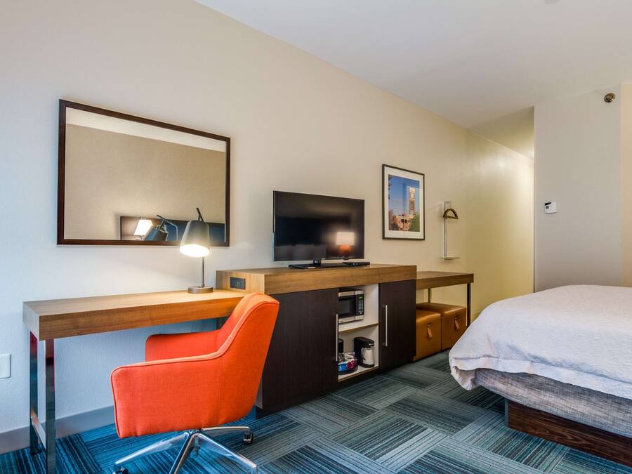 A hotel room with a bed, a desk with a chair, a television, a microwave, and a coffee maker.