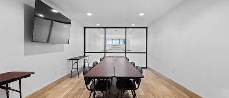 A conference room with a long table, chairs, a TV mounted on the wall, and a large window with a view.