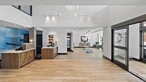 A spacious lobby with a wooden reception desk, a large wall mural, and a modern chandelier. - La Quinta Inn & Suites by Wyndham Santa Cruz (Santa Cruz)