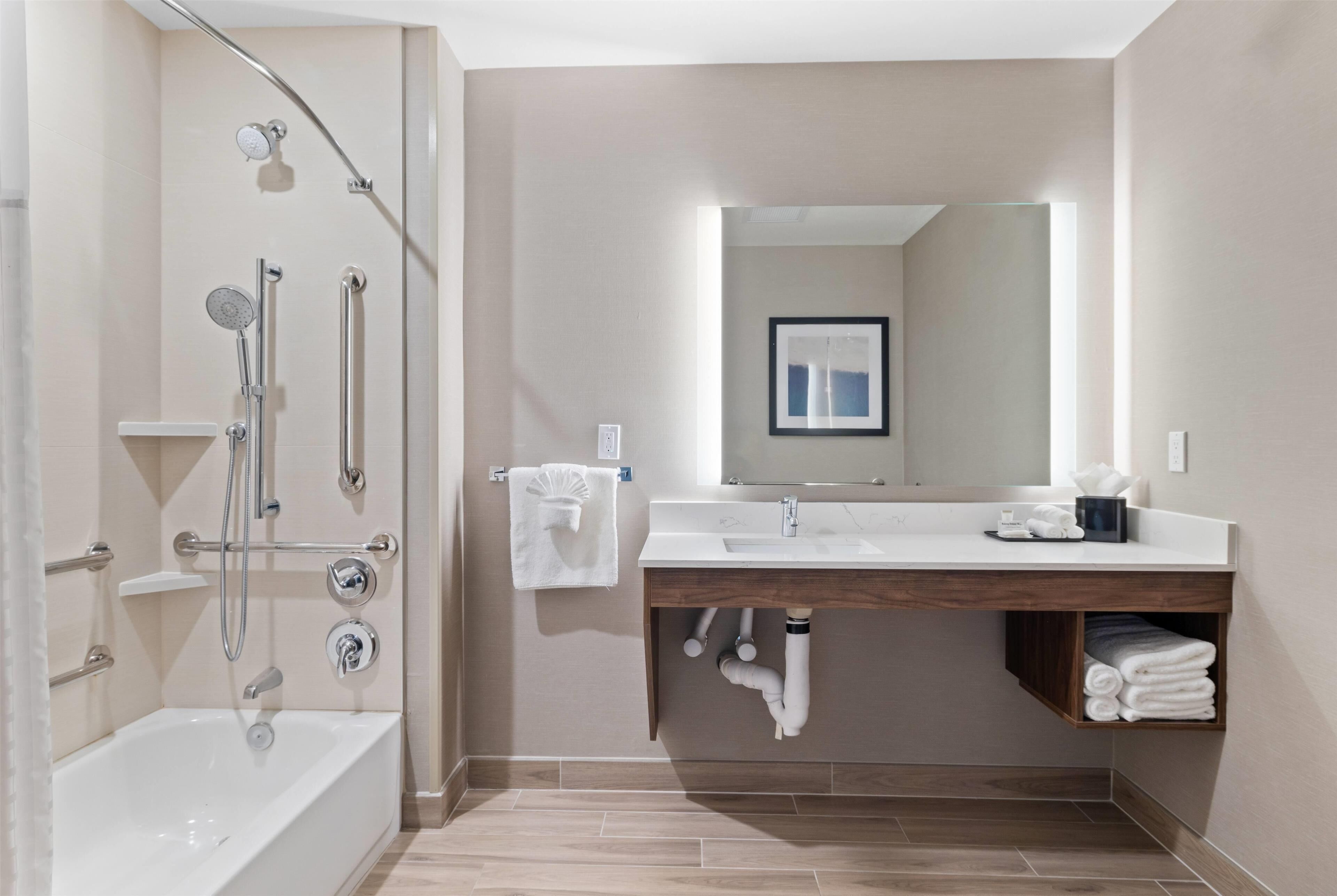 Een moderne badkamer met een badkuip, douche, wastafel met spiegel en een handdoekrek.
