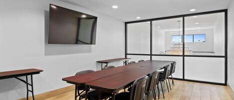 A conference room with a long wooden table, black chairs, and a large window with a view of the sky.