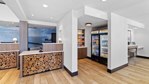 A modern reception area with a wooden log wall, a beverage refrigerator, and a view of the sea. - La Quinta Inn & Suites by Wyndham Santa Cruz (Santa Cruz)