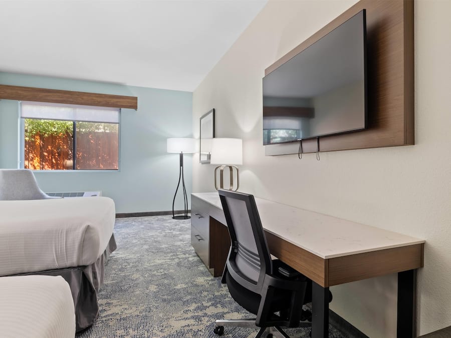 Une chambre d’hôtel équipée d’un lit, d’un bureau, d’une chaise, d’une télévision et d’une fenêtre avec des stores.