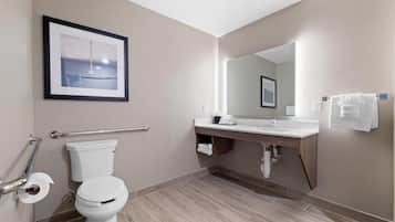 A modern bathroom with a toilet, handrail, sink, mirror, and towel rack.