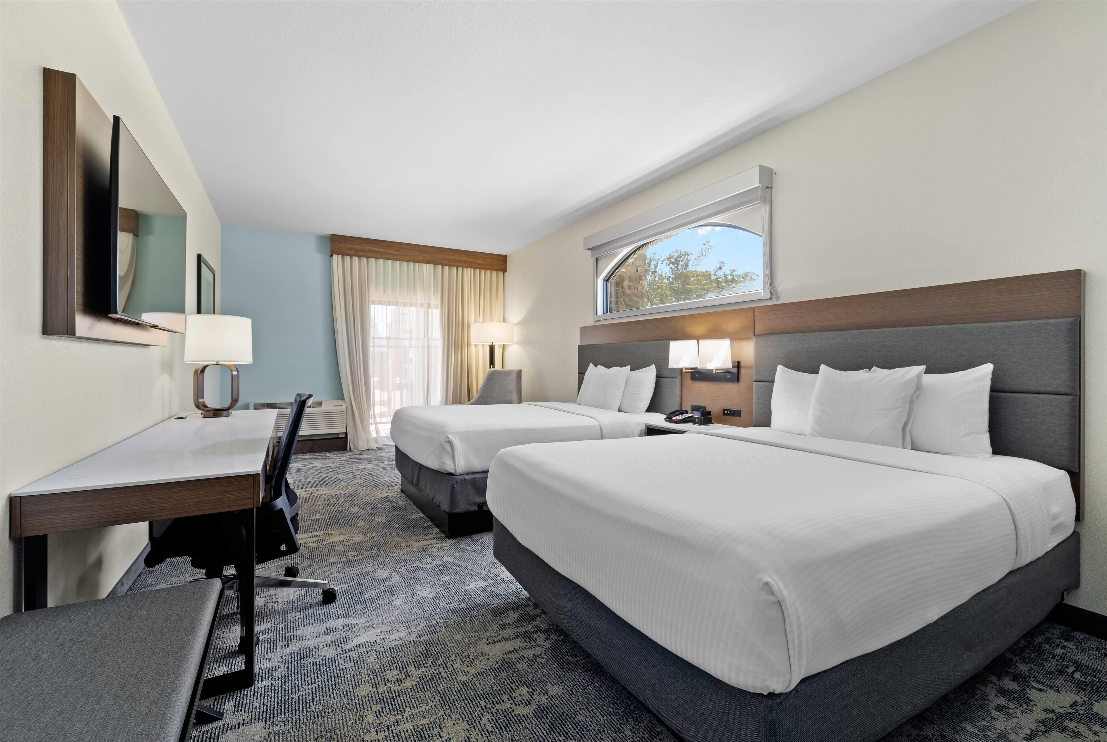 A hotel room with two beds, a desk, a chair, a TV, and a window with curtains.