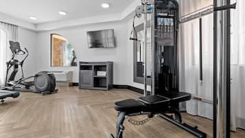 Et moderne fitnessrum med træningsudstyr, fjernsyn og et stort spejl.