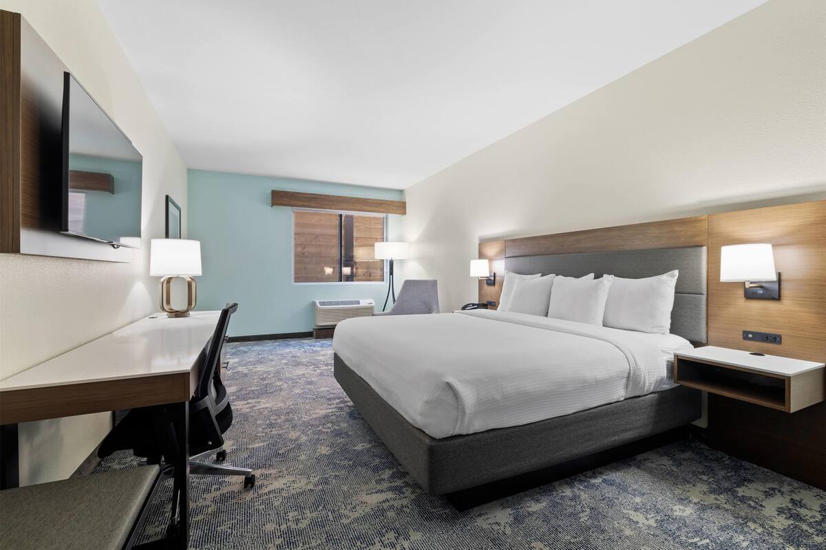 A hotel room with a bed, desk, chair, and nightstands.