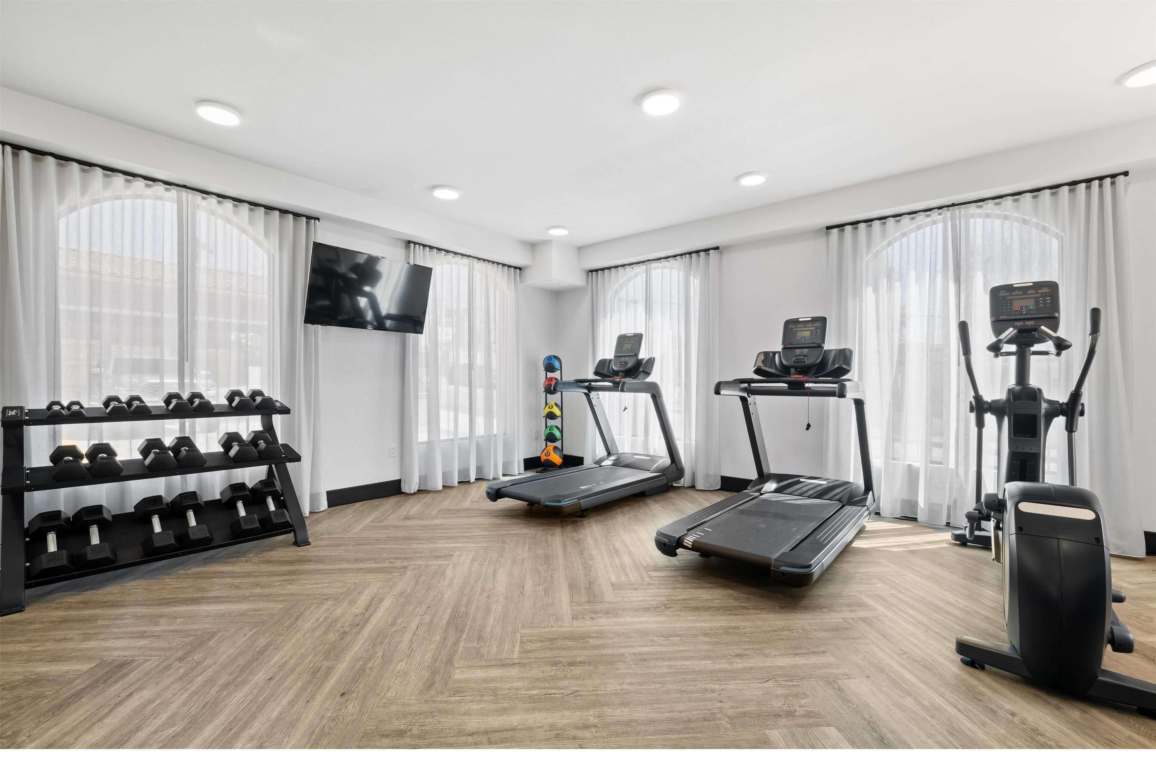 Une salle de sport moderne équipée de tapis de course, d’un vélo d’appartement et d’un banc de musculation.