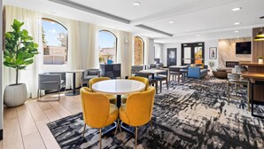 A modern hotel lobby with a round table, yellow chairs, a large potted plant, and a patterned carpet. - La Quinta Inn & Suites by Wyndham Santa Cruz (Santa Cruz)