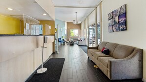 A hotel lobby with a reception desk, a sofa, a coffee table, and a wall with a cityscape artwork. - MC Pacific Inn & Suites (Torrance)