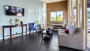 A modern living room with a dark wood floor, a flat-screen TV mounted on the wall, a sofa, a coffee table, and two chairs. - MC Pacific Inn & Suites (Torrance)