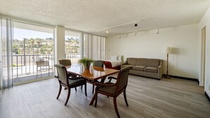 A spacious living room with a wooden dining table, two chairs, a sofa, and a lamp. - MC Pacific Inn & Suites (Torrance)